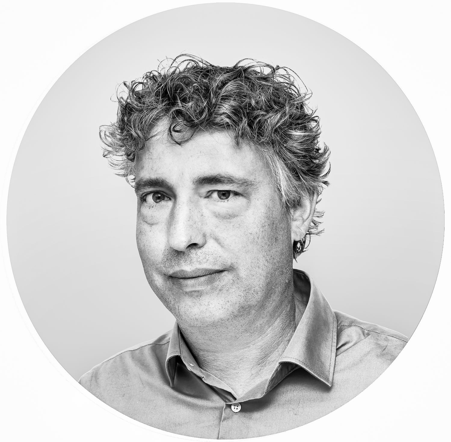Black and white professional headshot portrait of curly haired person in light colored shirt against plain background.