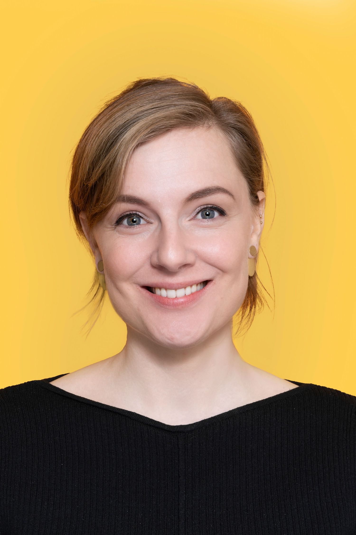 Professional portrait of a person wearing a black top against a bright yellow background, smiling warmly at the camera.