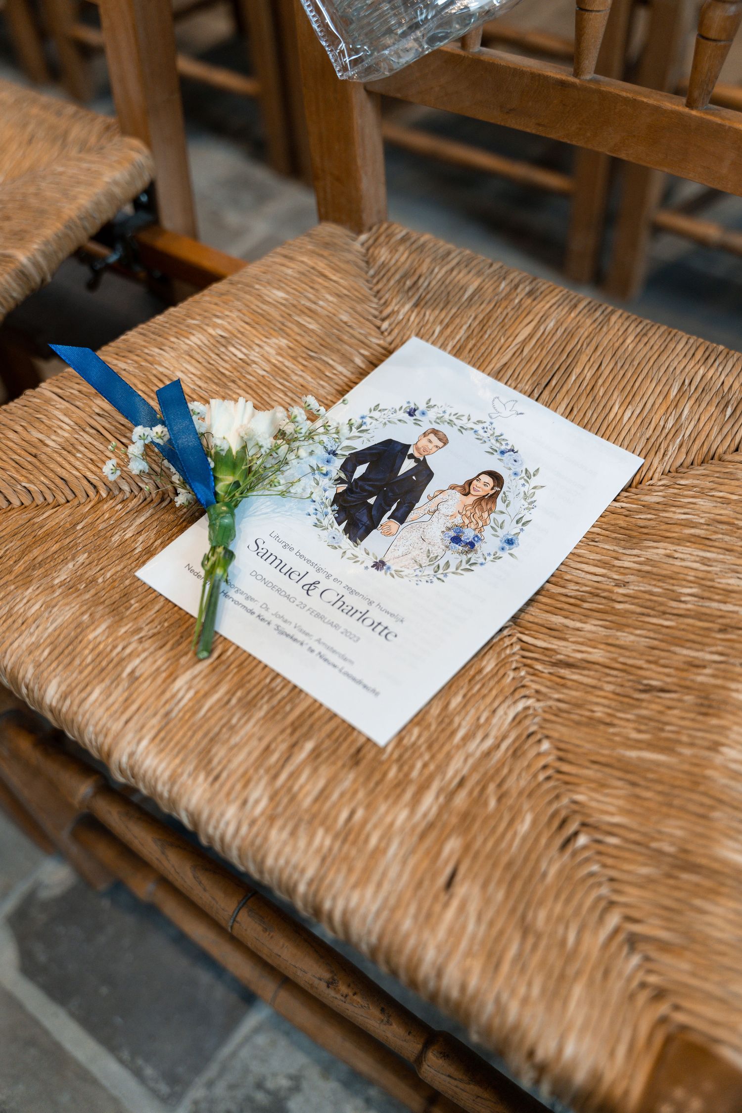 Wedding program with illustrated couple design and blue flower decoration on a wooden chair.