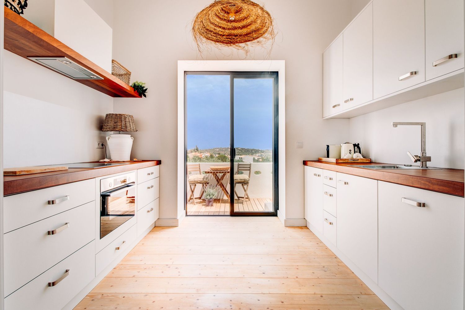 Modern white galley kitchen with wooden countertops and sliding door leading to outdoor terrace.