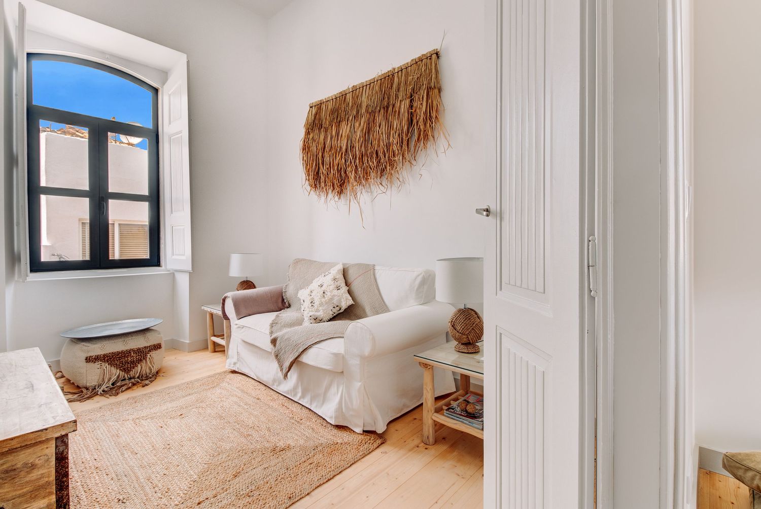 Minimalist sitting area with white couch, jute rug, and macrame wall hanging.