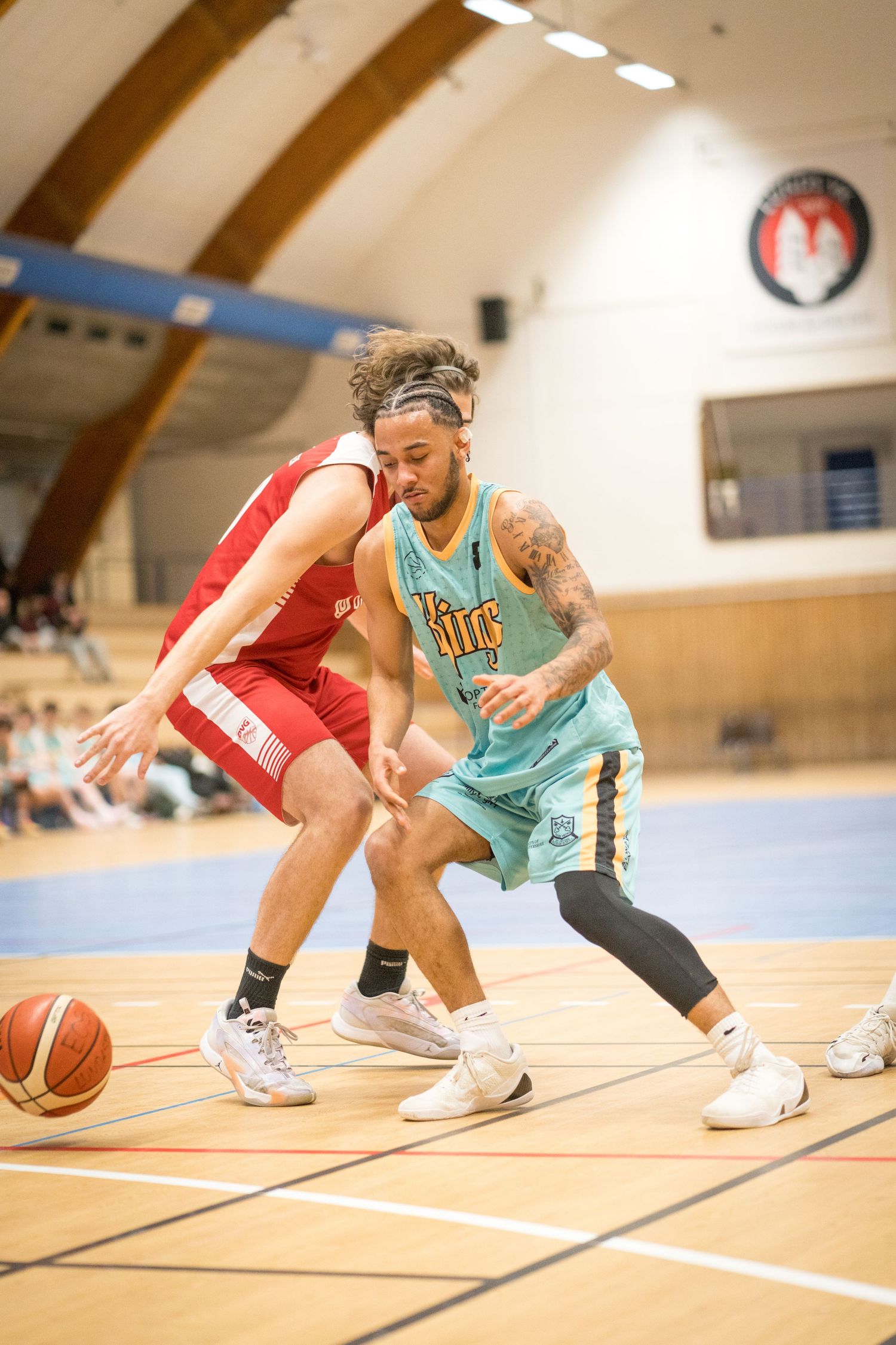 Basketball players from opposing teams compete for possession during an indoor game on a wooden court.