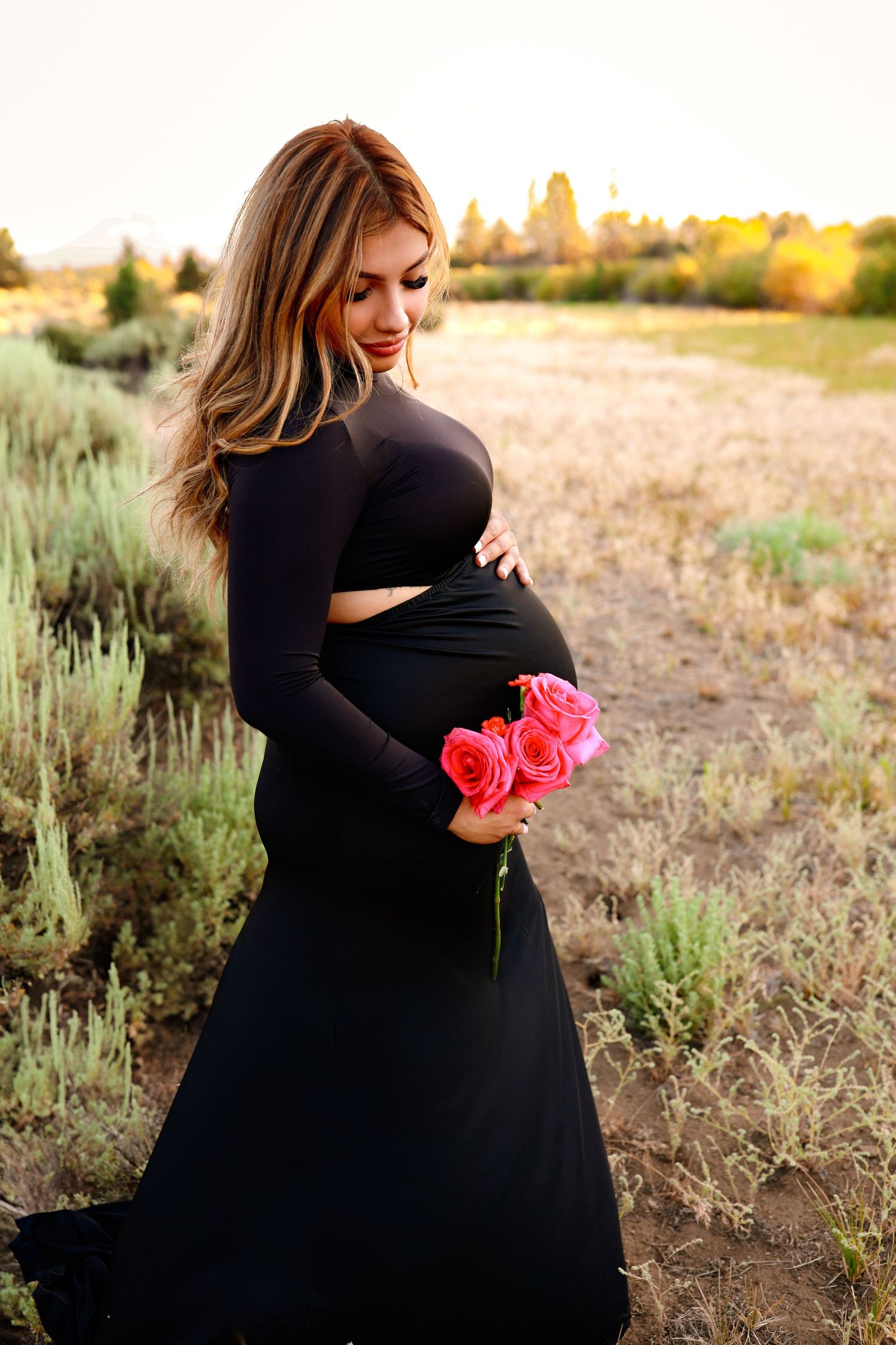 A maternity photoshoot in a field at sunset shows five progressive poses with pink flowers and a black dress.