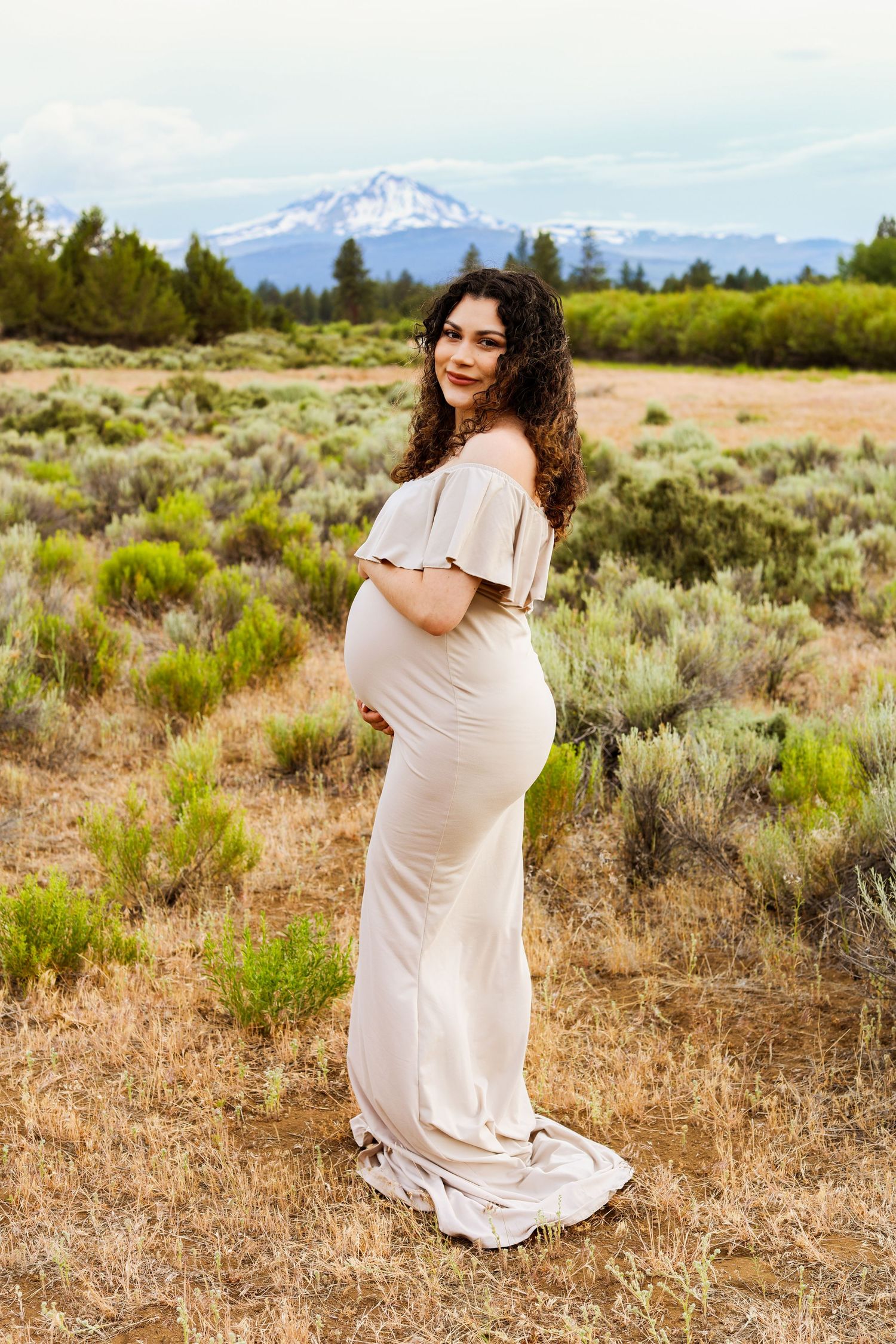 Maternity photo in a blush dress with snow-capped mountain views and sagebrush fields in Central Oregon.