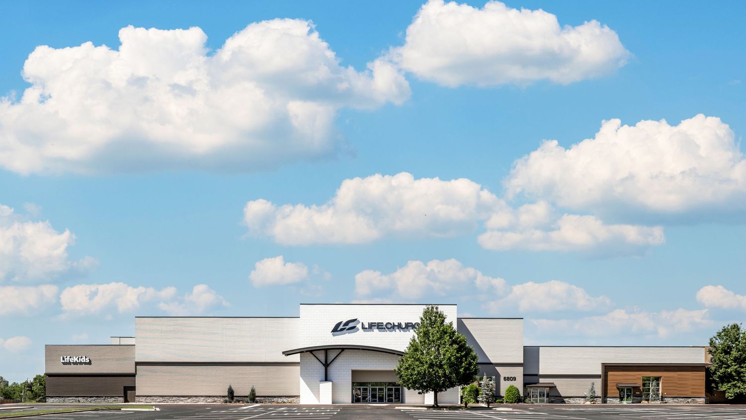 Modern church building exterior with white walls and clean architectural lines against a blue sky with puffy clouds.