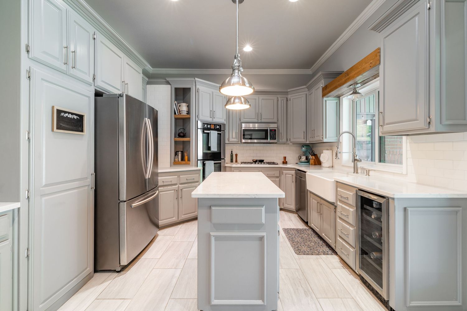 Modern white kitchen with stainless appliances features dual islands, custom cabinetry, and pendant lighting.