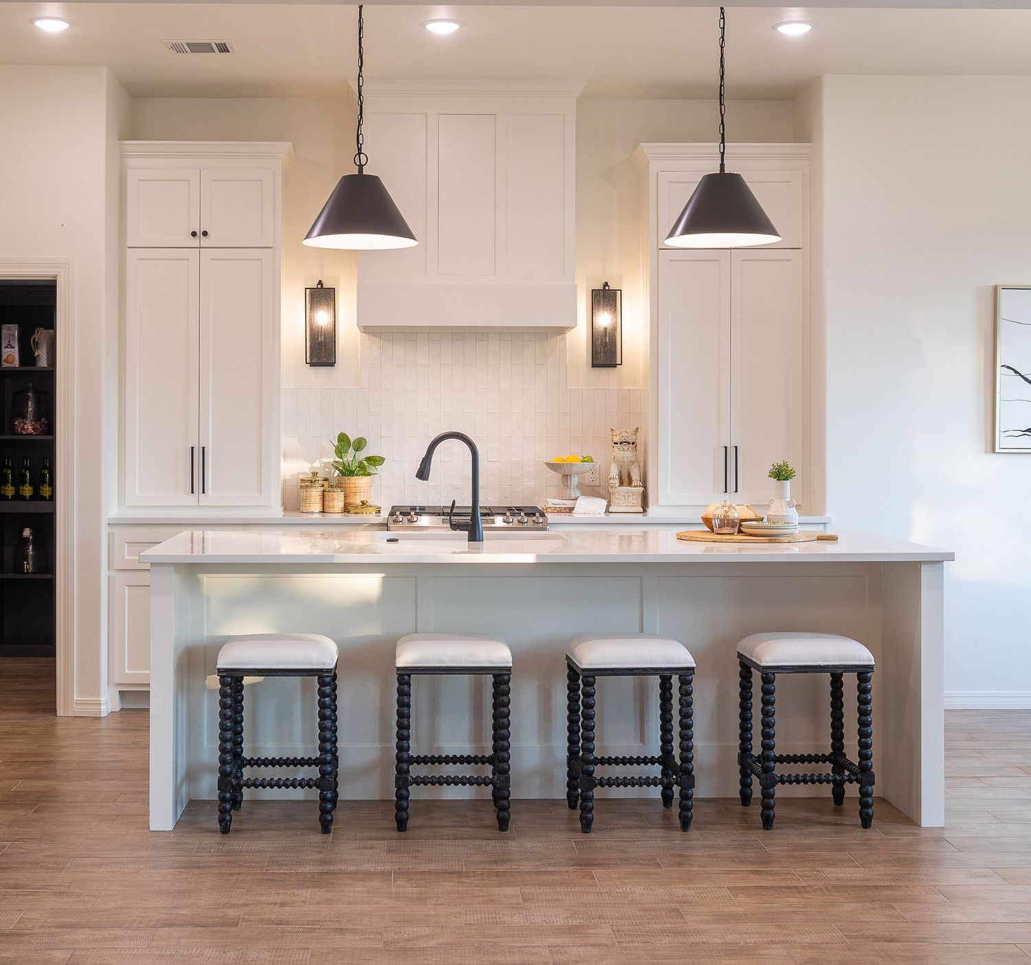 Modern white kitchen with large island, pendant lights, bar stools, and hardwood floors in a minimalist design style.