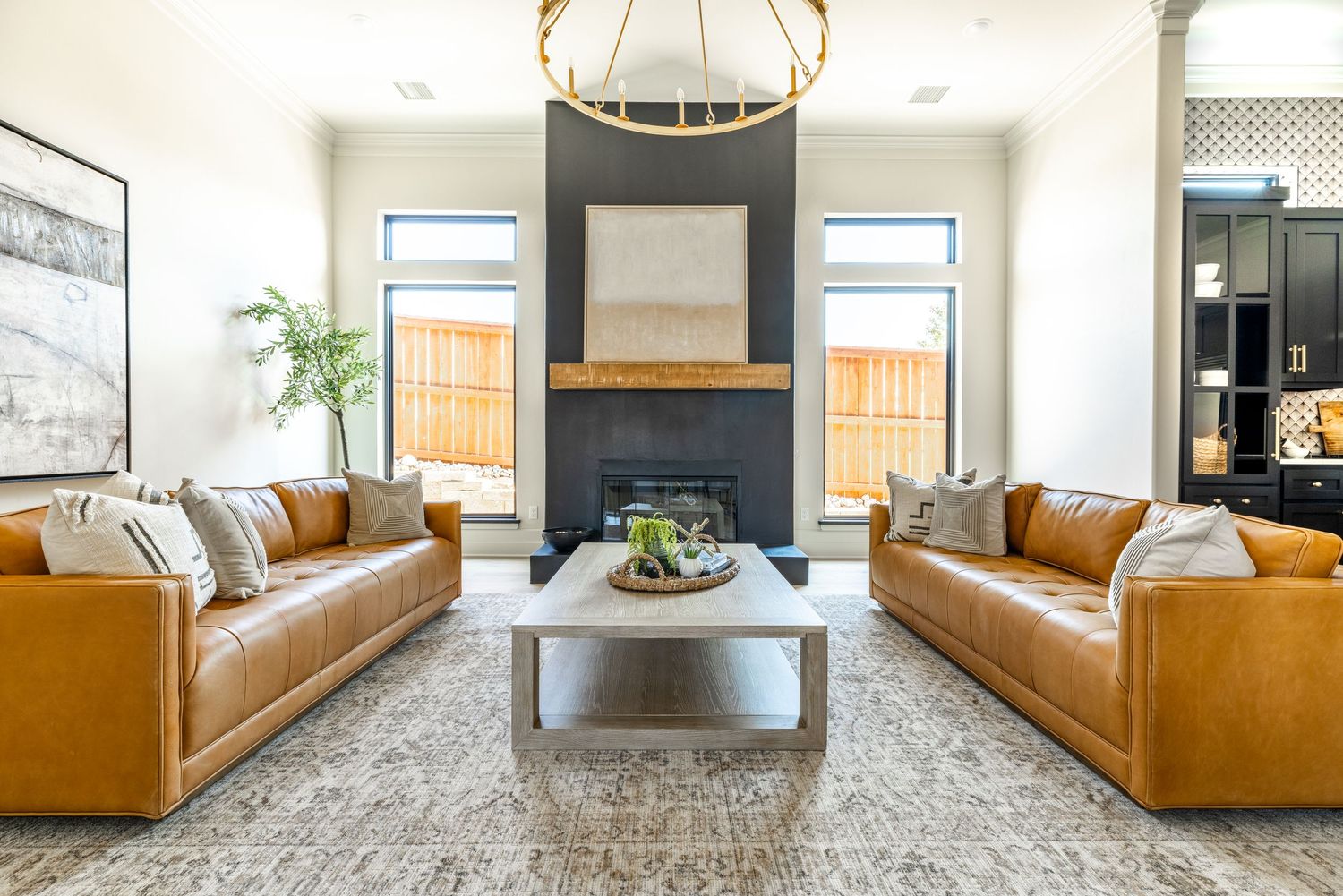 Modern living room with tan leather sofas, grey fireplace, and contemporary light fixture in bright open space.