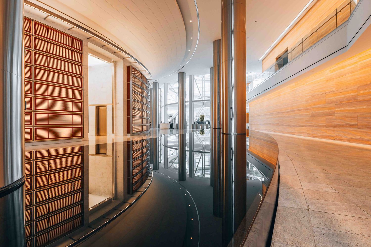 Elegant curved hallway with reflective floors and wooden wall panels in contemporary building design.