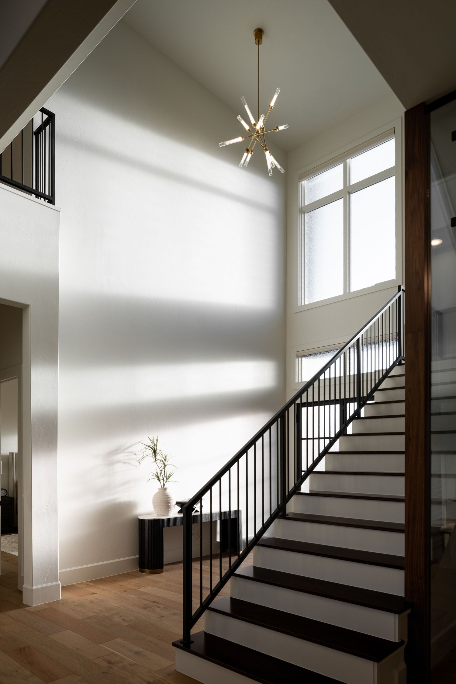 Modern staircase with black metal railings and light hardwood steps illuminated by a contemporary sputnik chandelier.