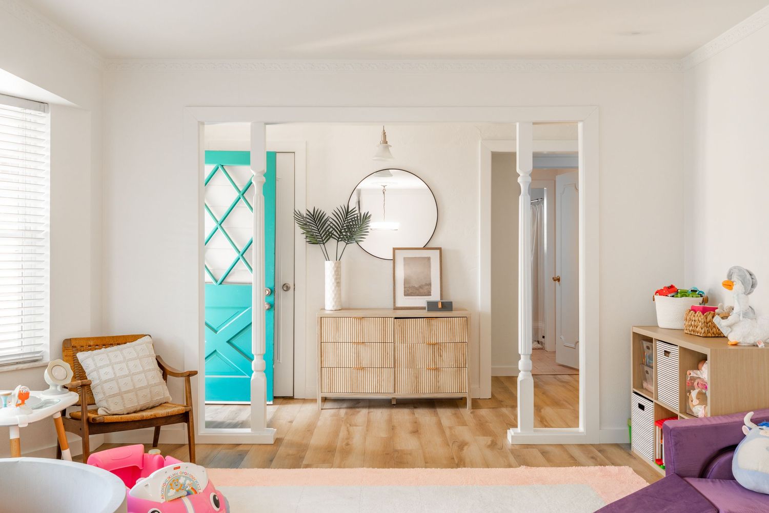 Modern interior room featuring turquoise door, light wood floors, rattan chair, and natural decor elements.