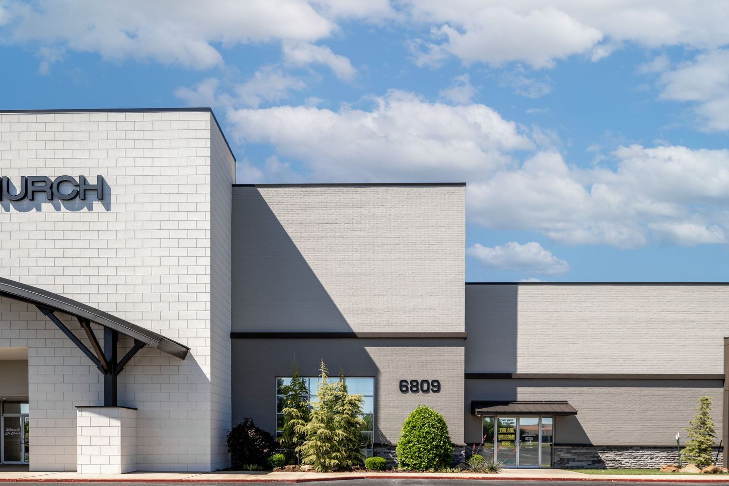Contemporary white brick church entrance with glass doors and architectural details under blue skies.