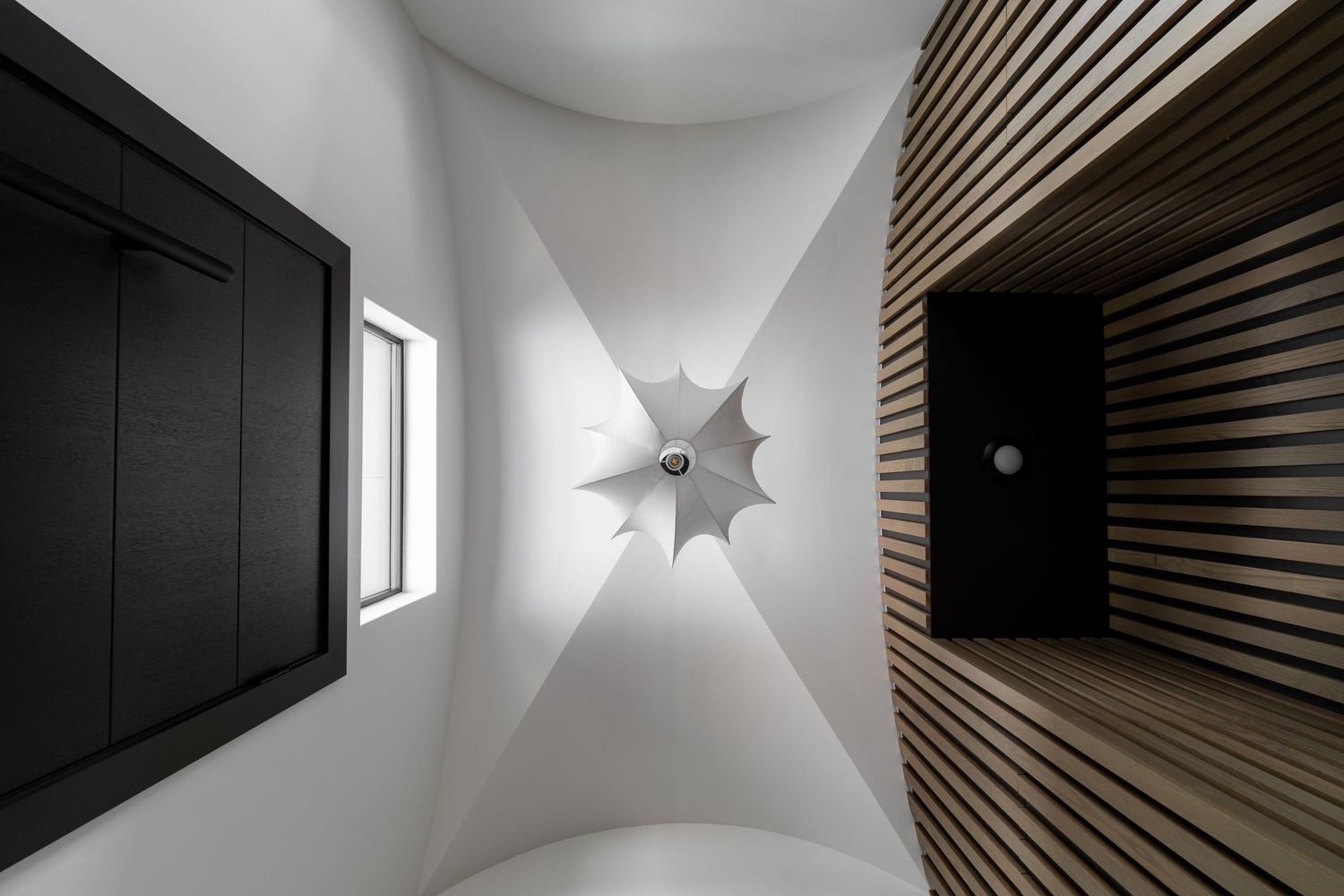 Modern corridor with white walls and dark wooden slats creating dramatic angular lighting patterns and shadows.