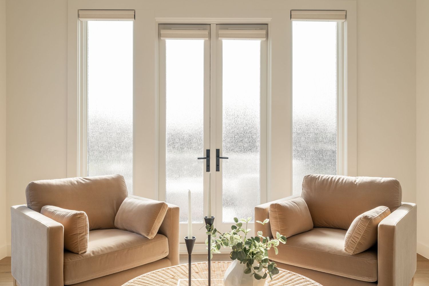 Two beige armchairs facing each other in front of large French doors with natural light streaming in.