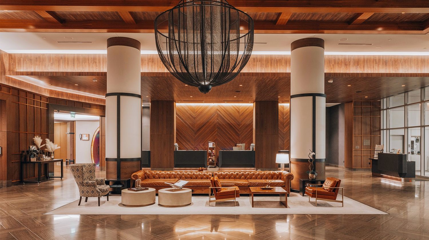 Contemporary hotel lobby with wood ceiling, white columns, and brown leather sectional seating.