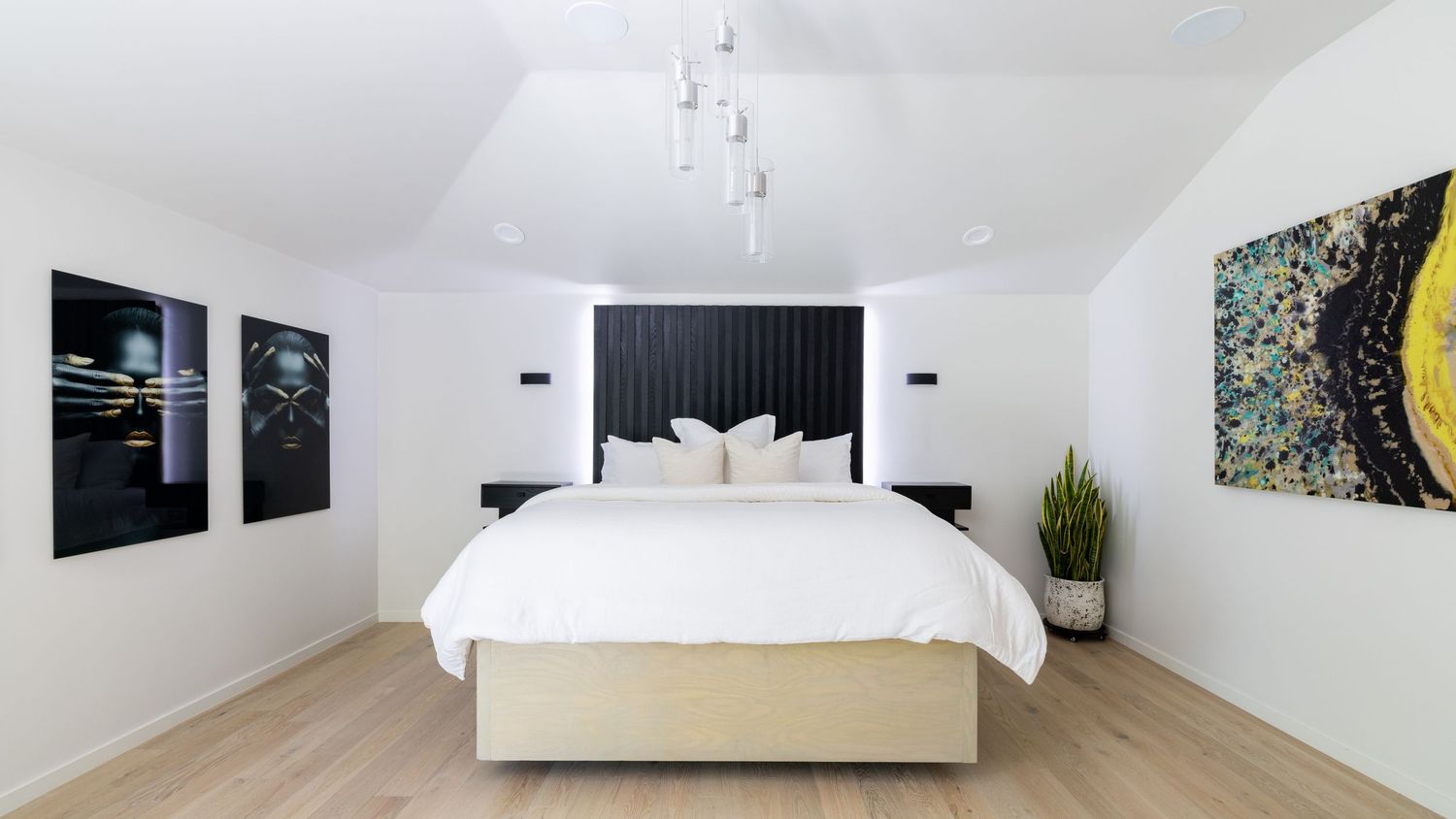 Modern minimalist bedroom with white bedding, black headboard, and abstract wall art in a clean white space.