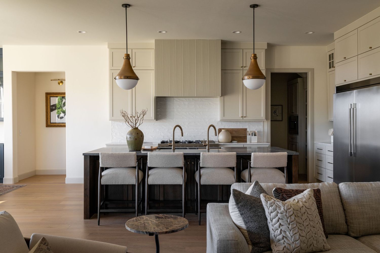 Modern open concept living space features sleek kitchen with pendant lights, island seating, and plush gray sectional sofa.