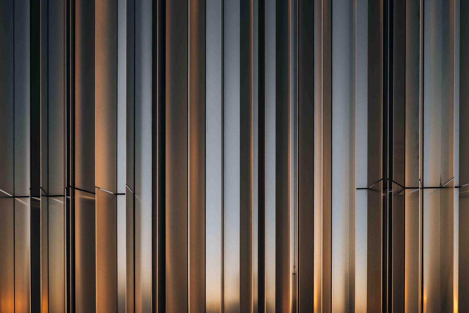 Geometric metal wall art with vertical lines creating a striped pattern in metallic tones at sunset.