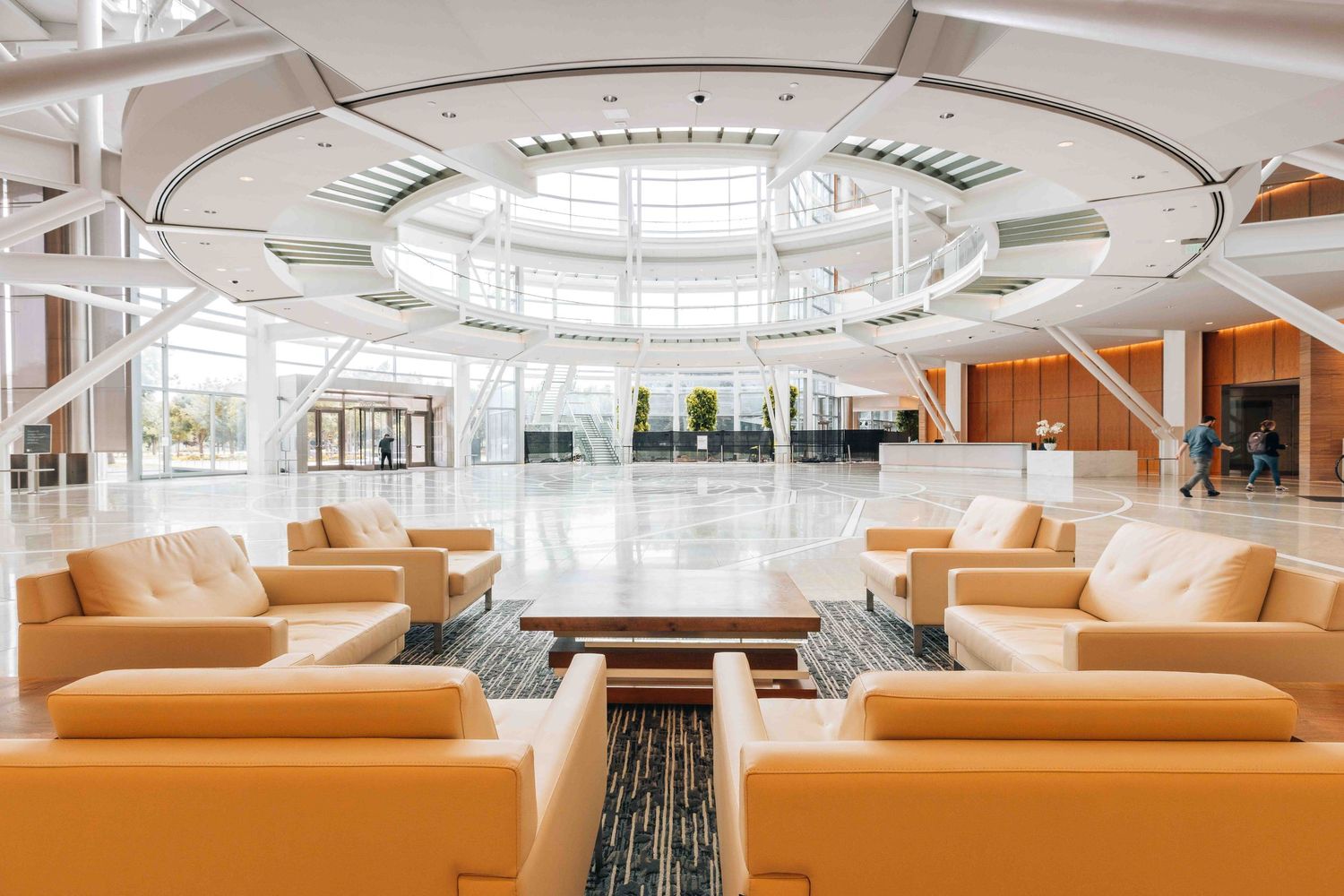 Luxurious modern lobby interior with orange leather couches arranged in circular formation under skylight.