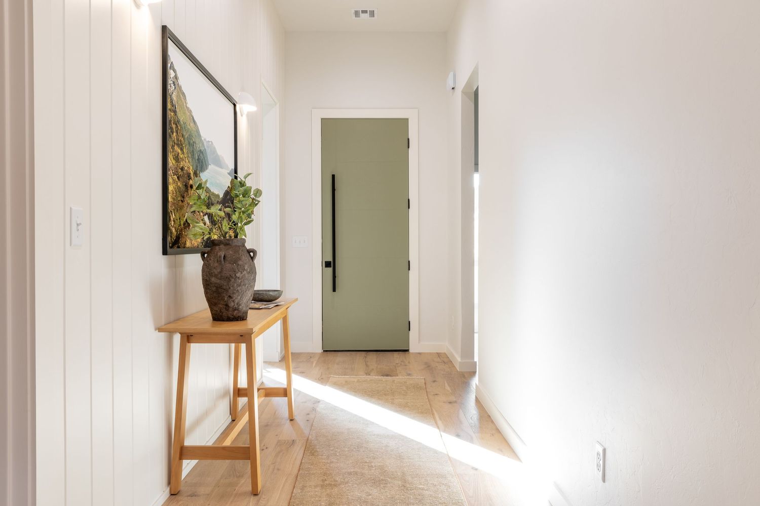 Bright modern hallway with white walls features a wooden console table, potted plant, and natural light streaming through.