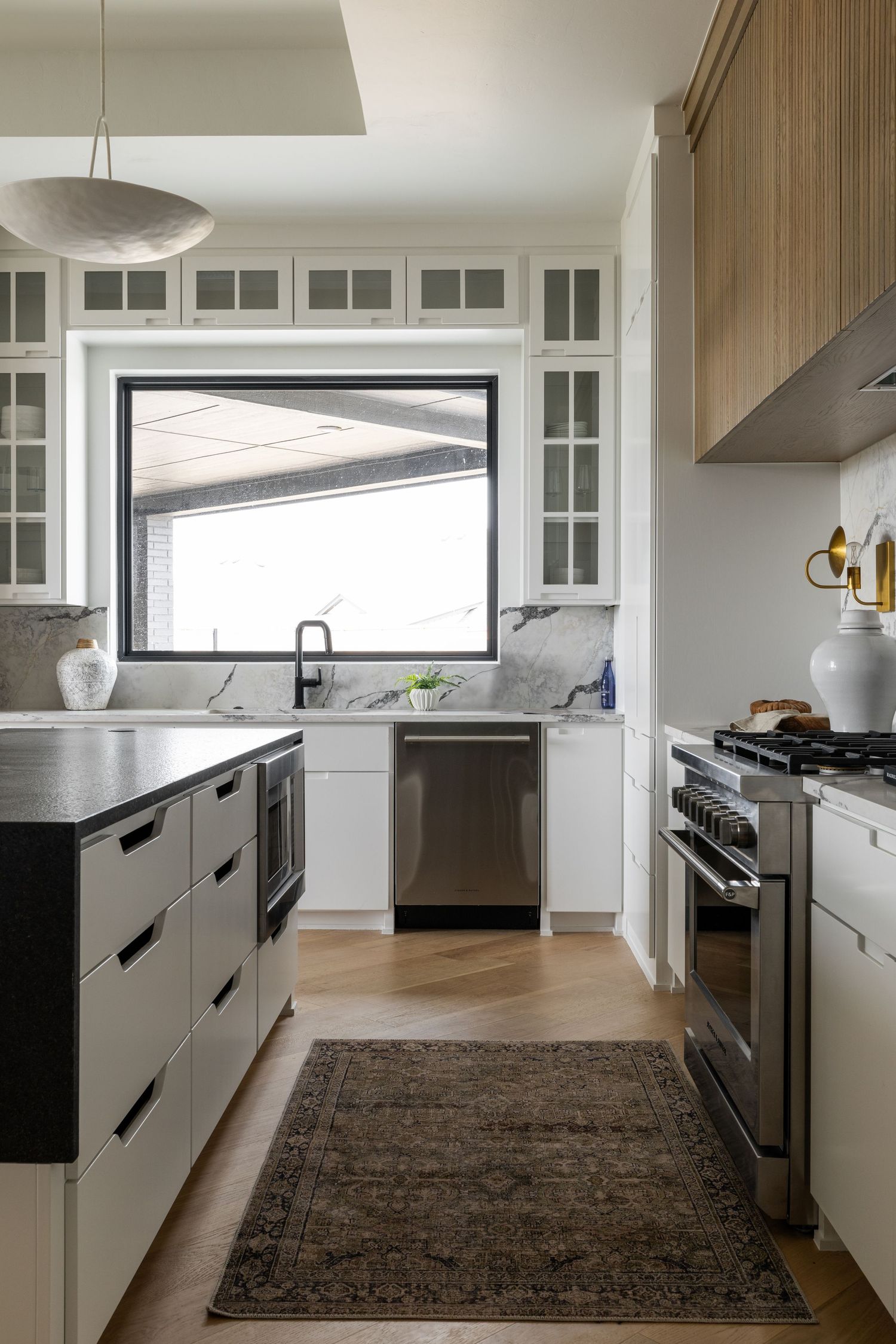 Modern white kitchen with black base cabinets, marble backsplash, glass upper cabinets, and stainless steel appliances.