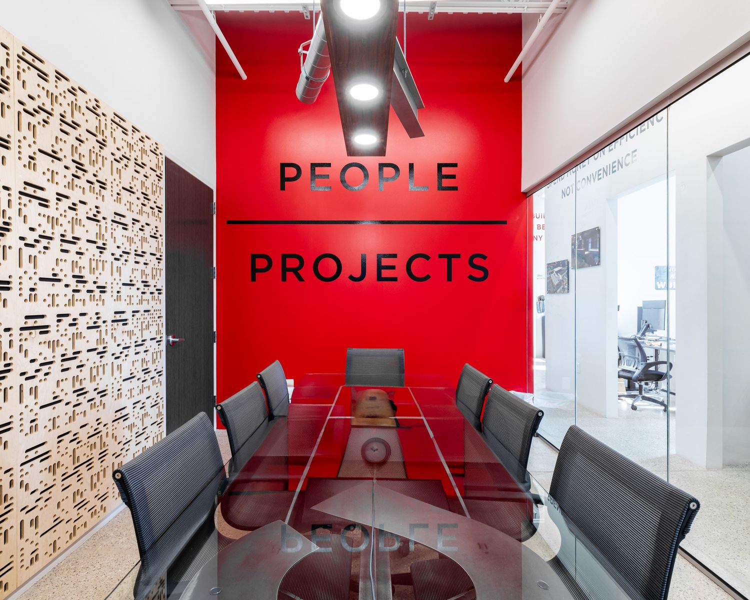 Modern conference room with glass table, black chairs, red accent wall and decorative wood panel wall design.