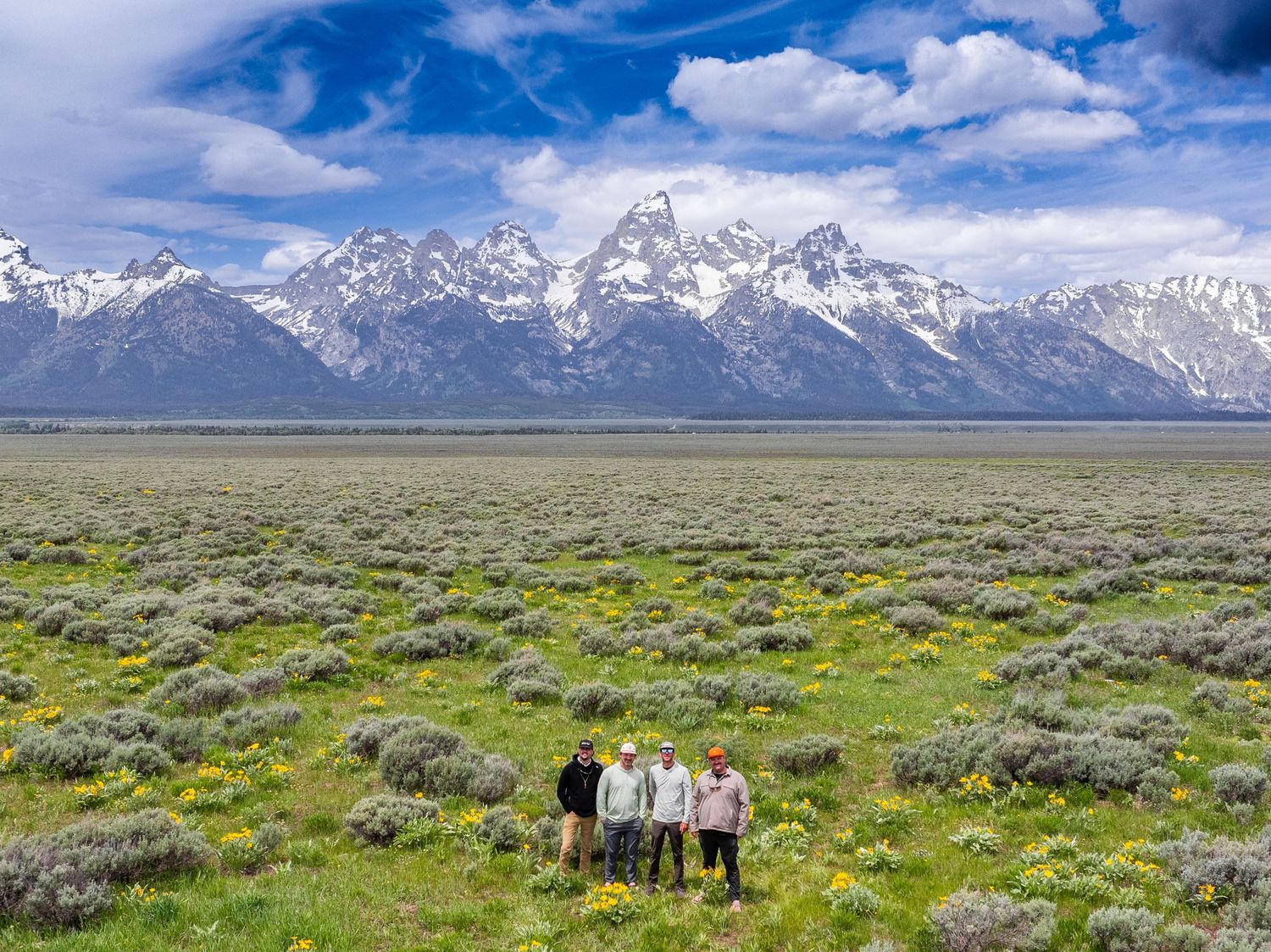 A group stands in a vast sagebrush plain beneath the majestic snow-capped peaks of Grand Teton National Park.