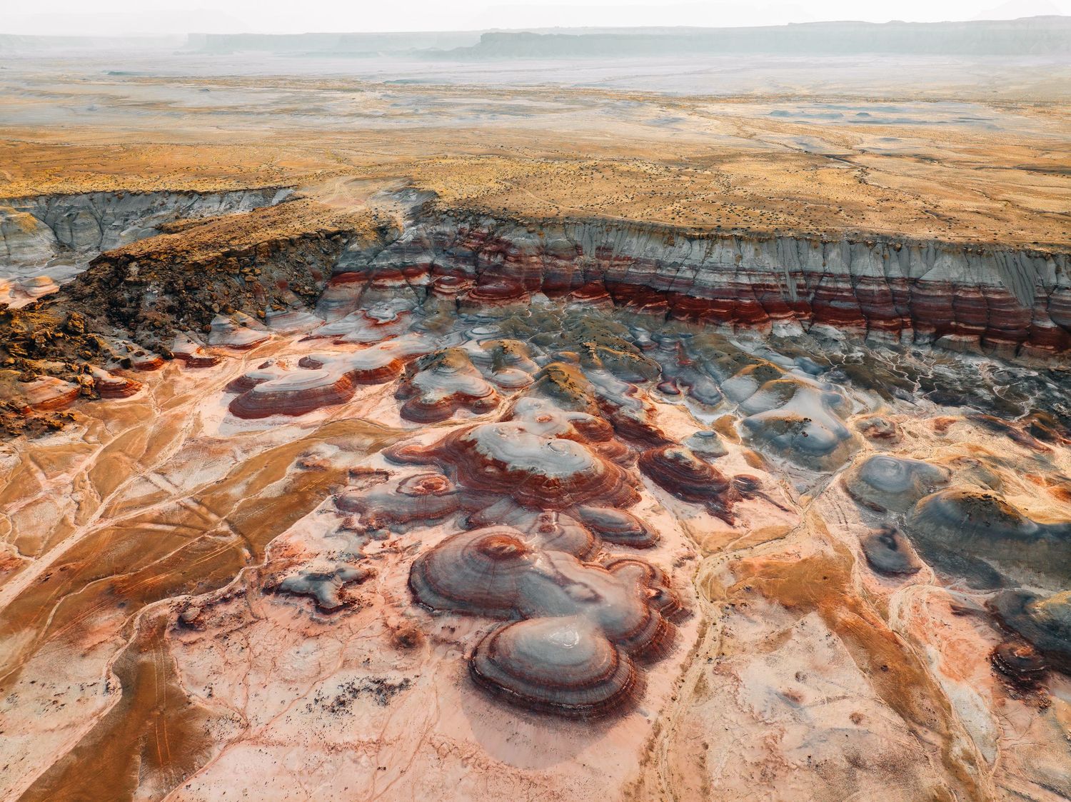 Aerial view of colorful geothermal pools and mineral deposits in a volcanic landscape with brown earth tones.