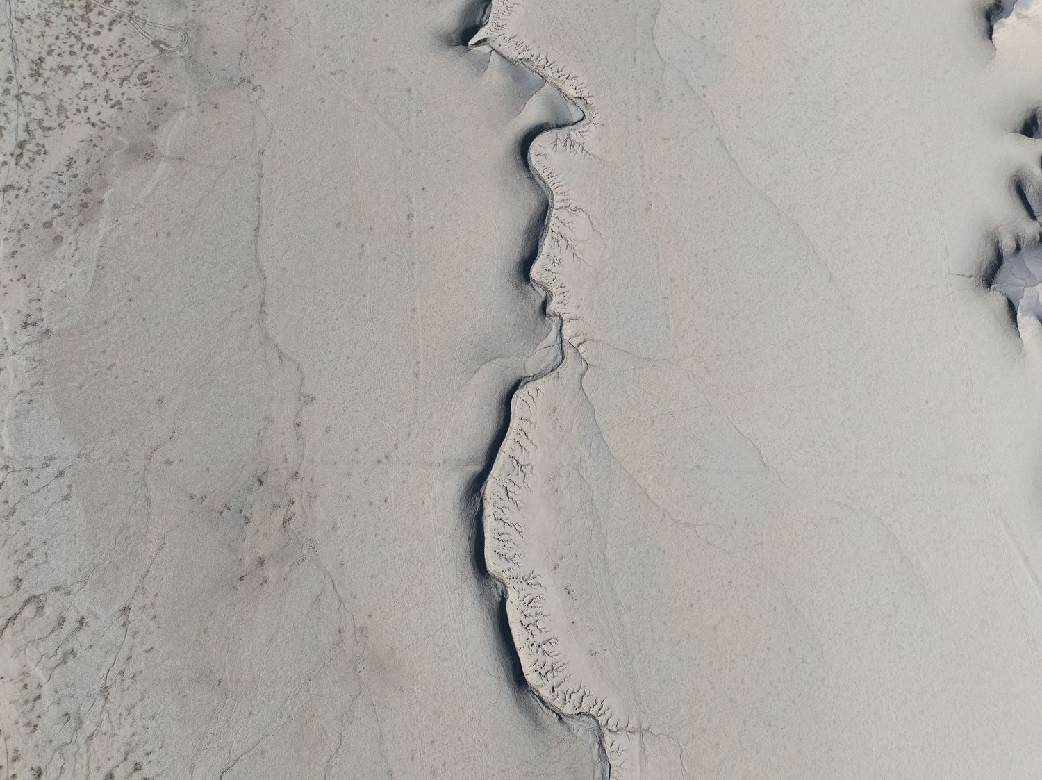 Aerial view of a winding river canyon with snow-covered banks creating a dramatic serpentine pattern across the landscape.
