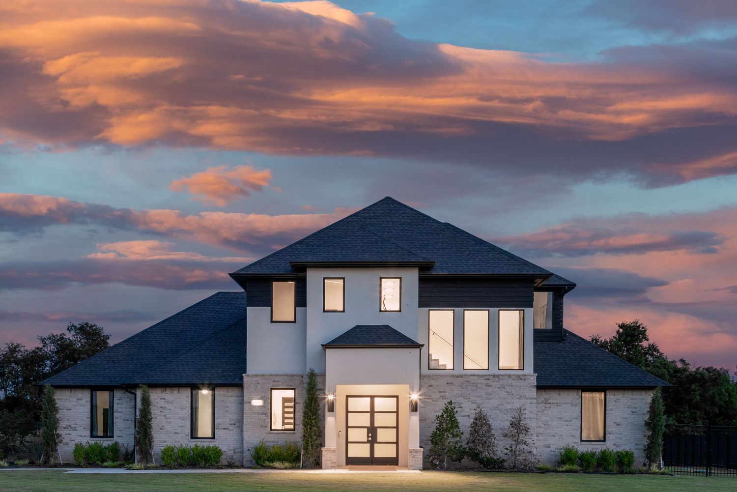 Modern luxury home exterior with dramatic pink and purple sunset clouds in the background during dusk.