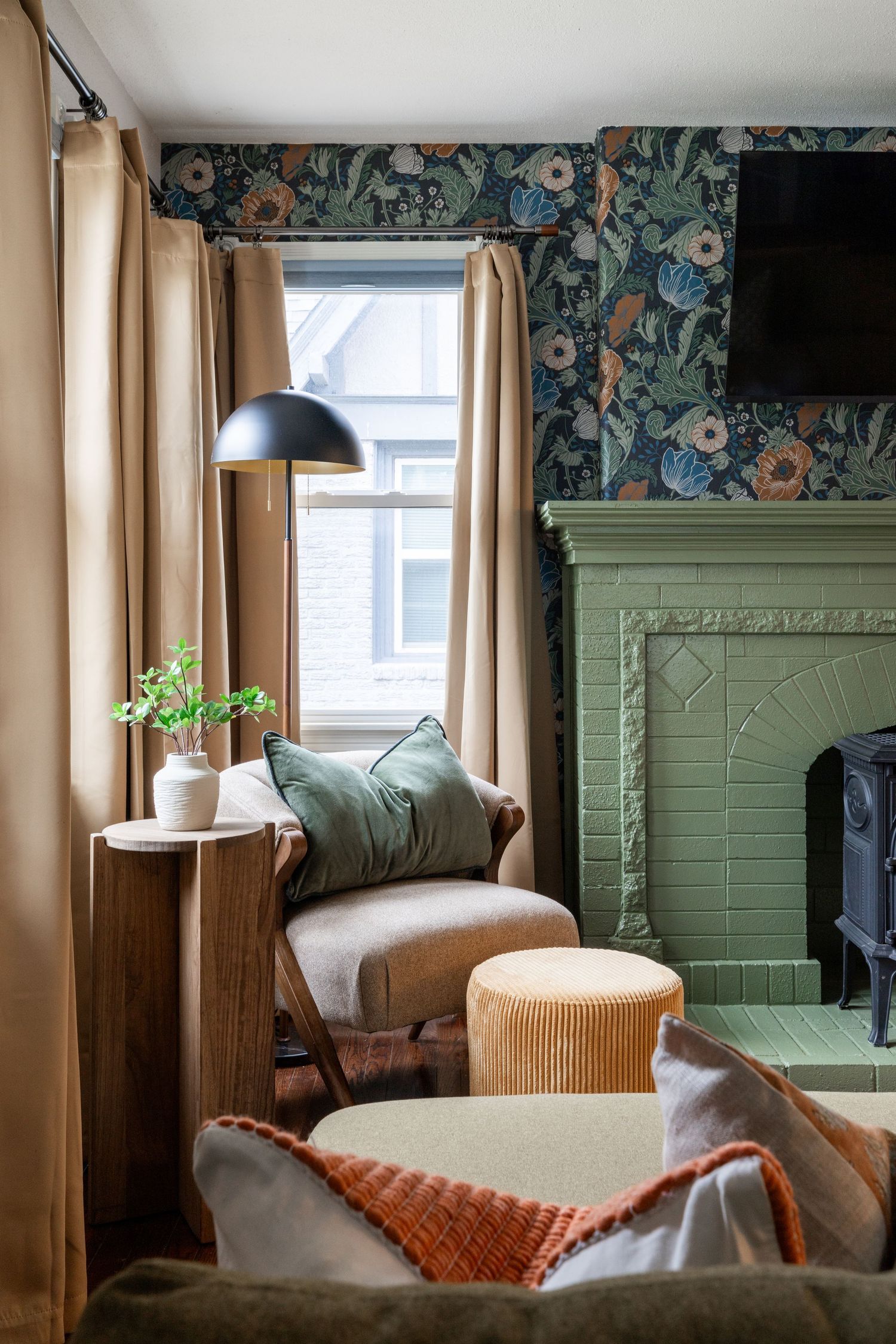 Cozy living room with floral wallpaper, sage green fireplace, beige curtains, and contemporary furniture and lighting.