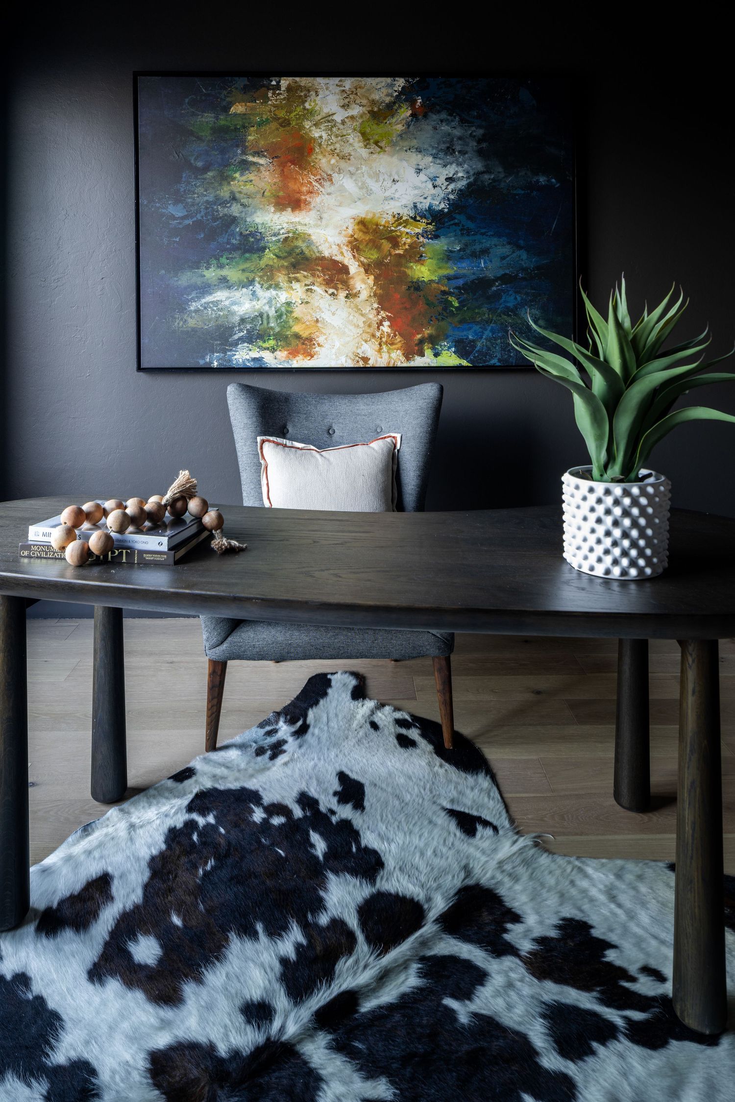 Modern living room with abstract art, cowhide rug, dark dining table, potted plant and contemporary decor details.