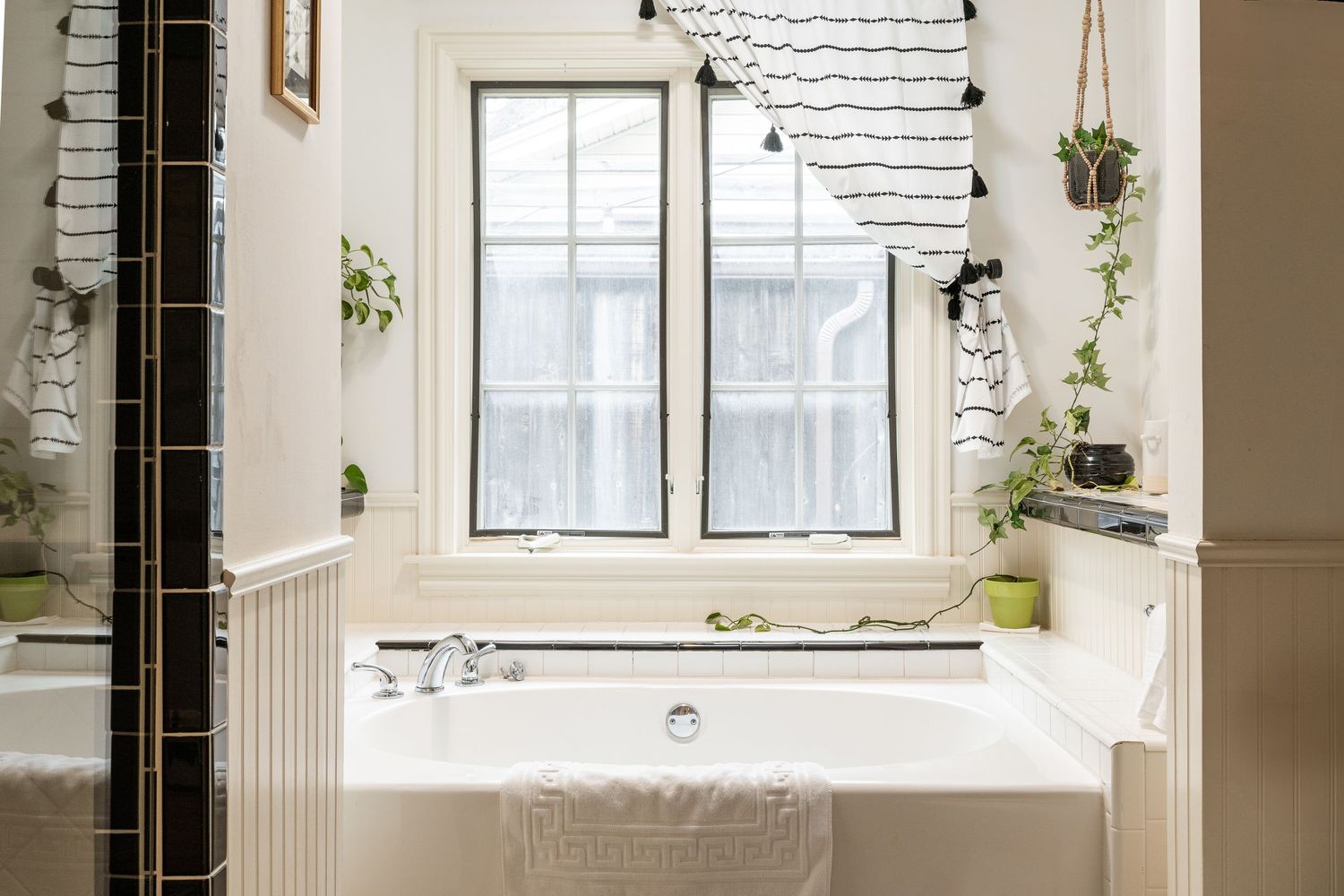 Bright white bathroom with vintage clawfoot tub, twin windows, and hanging plants creating a serene, minimalist atmosphere.