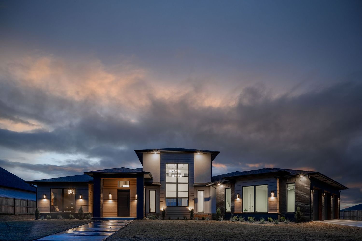 Modern luxury home exterior with dramatic lighting and storm clouds at dusk features contemporary architecture and glass walls.