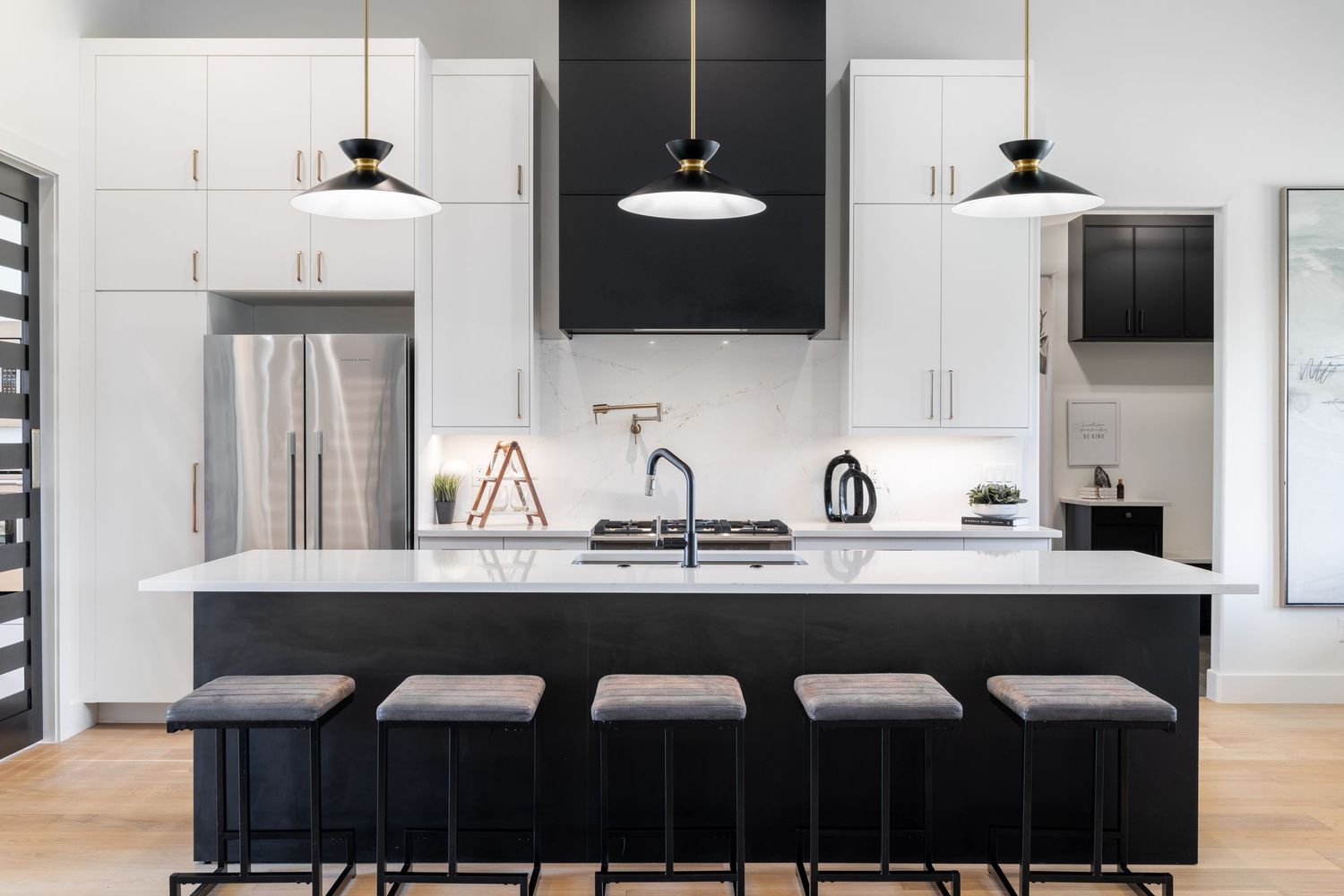 Modern kitchen features sleek black cabinetry, white walls, and pendant lighting in an open-concept design.