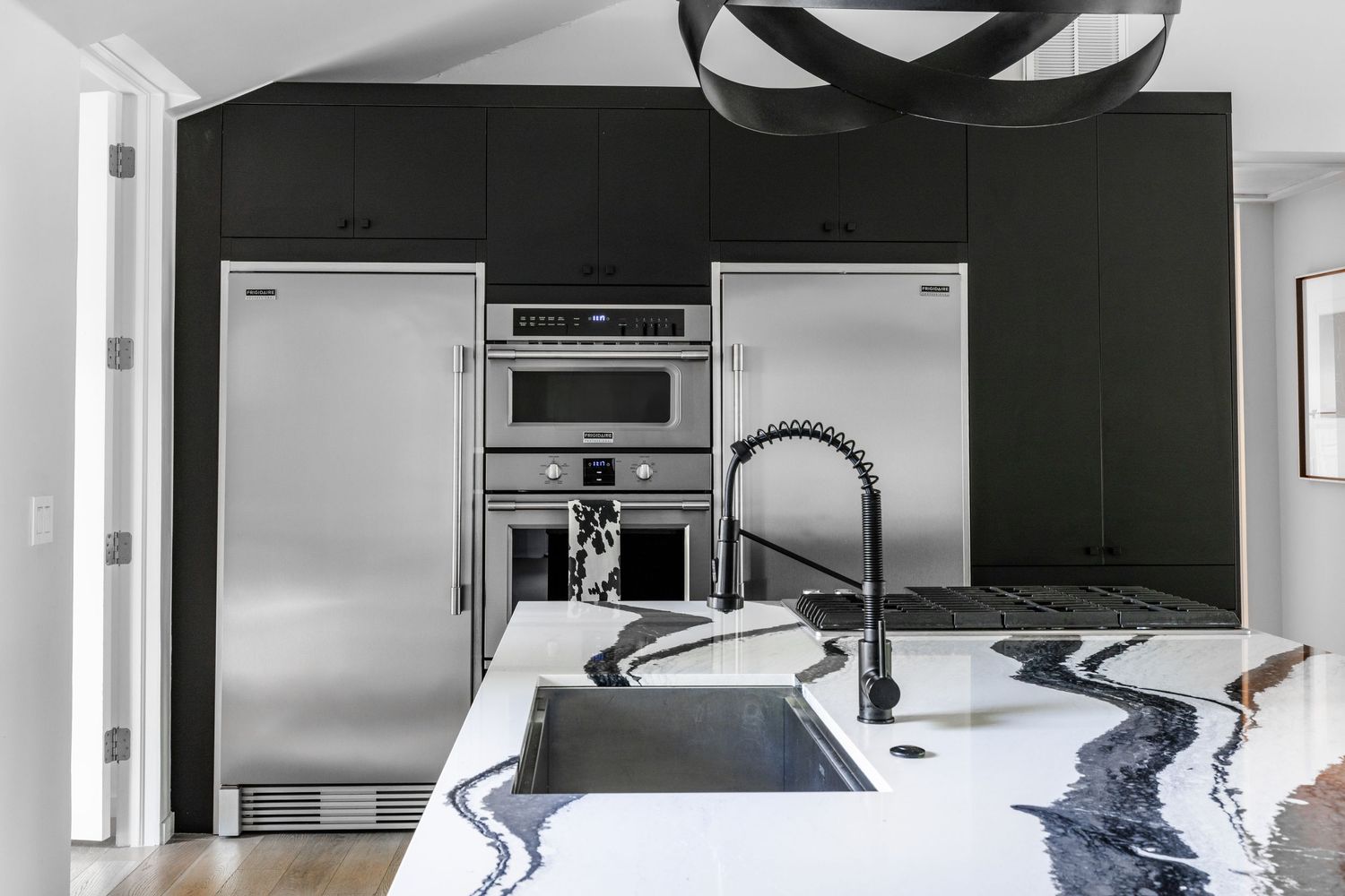 Contemporary kitchen featuring dark cabinetry, marble countertops, and professional-grade stainless steel appliances.