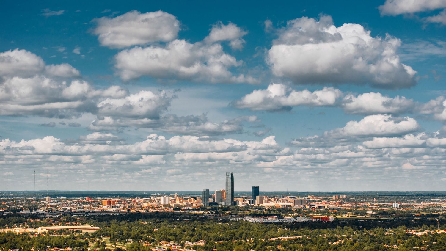 Aerial cityscape of Boston with iconic Prudential and Hancock towers under puffy white clouds and blue summer sky.