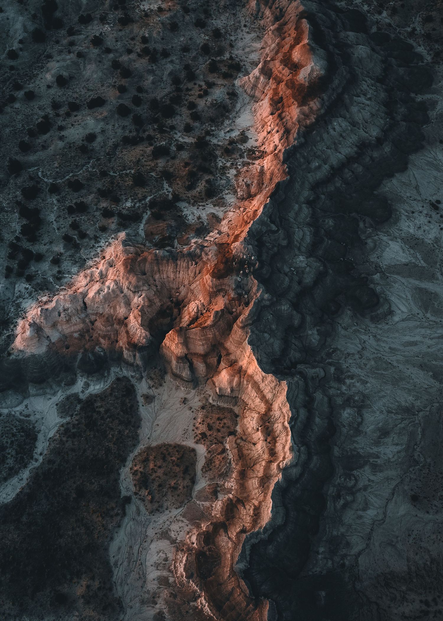 Aerial view of rocky mountain ridge illuminated by warm sunlight against dark shadows at sunset.