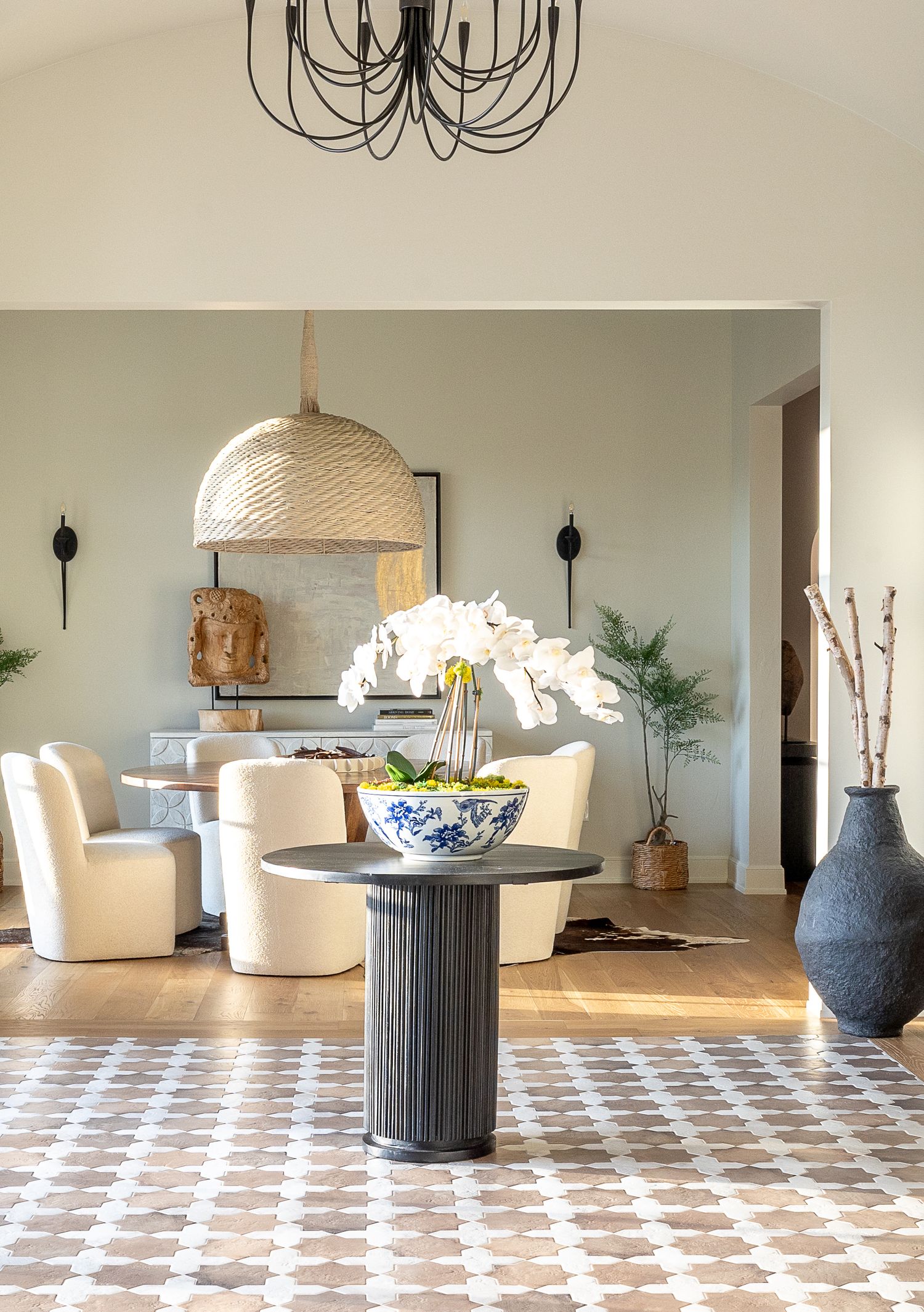 Modern living room with woven dome pendant light, cream chairs, geometric patterned rug, and decorative blue and white vase.