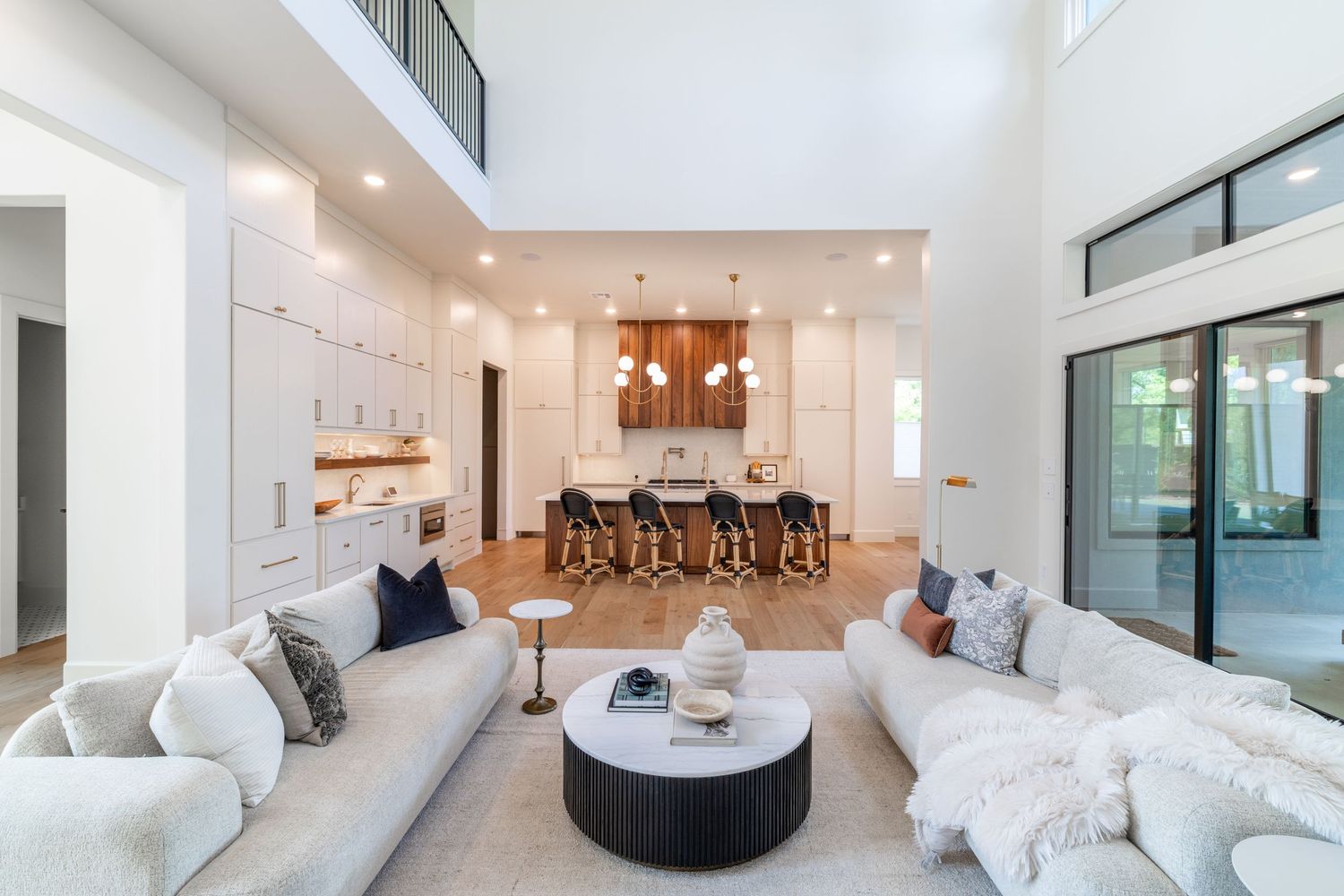 Modern luxurious open concept living room with high ceilings features white sectional sofa and adjacent kitchen with bar seating.