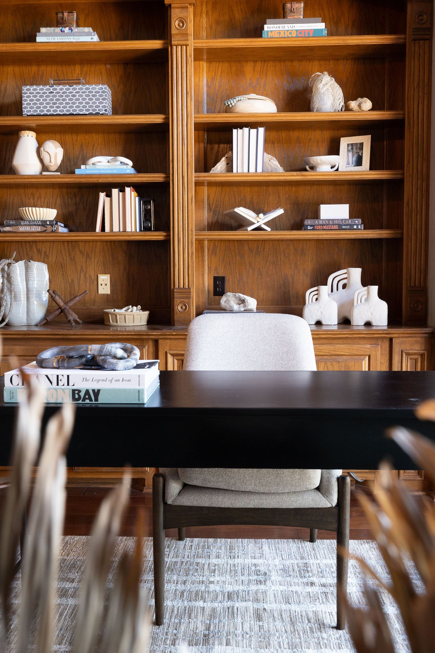 Modern home office features wooden built-in bookshelves styled with decor, books and a black desk with gray chair.