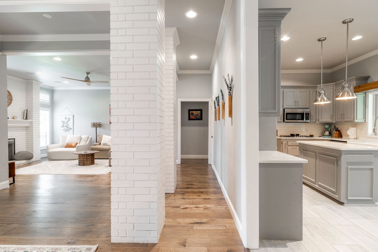 Modern open concept home interior with white brick column, hardwood floors, and gray kitchen cabinetry.