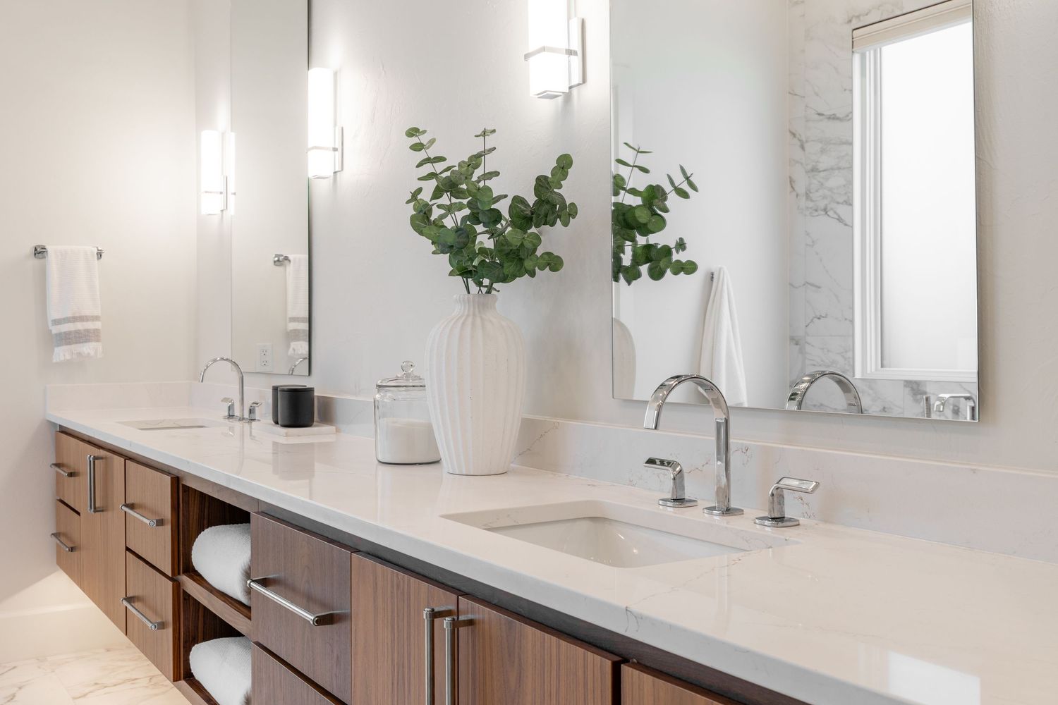 Contemporary bathroom vanity with double sinks, wooden cabinets, and white vessel bowl featuring green plant decor.