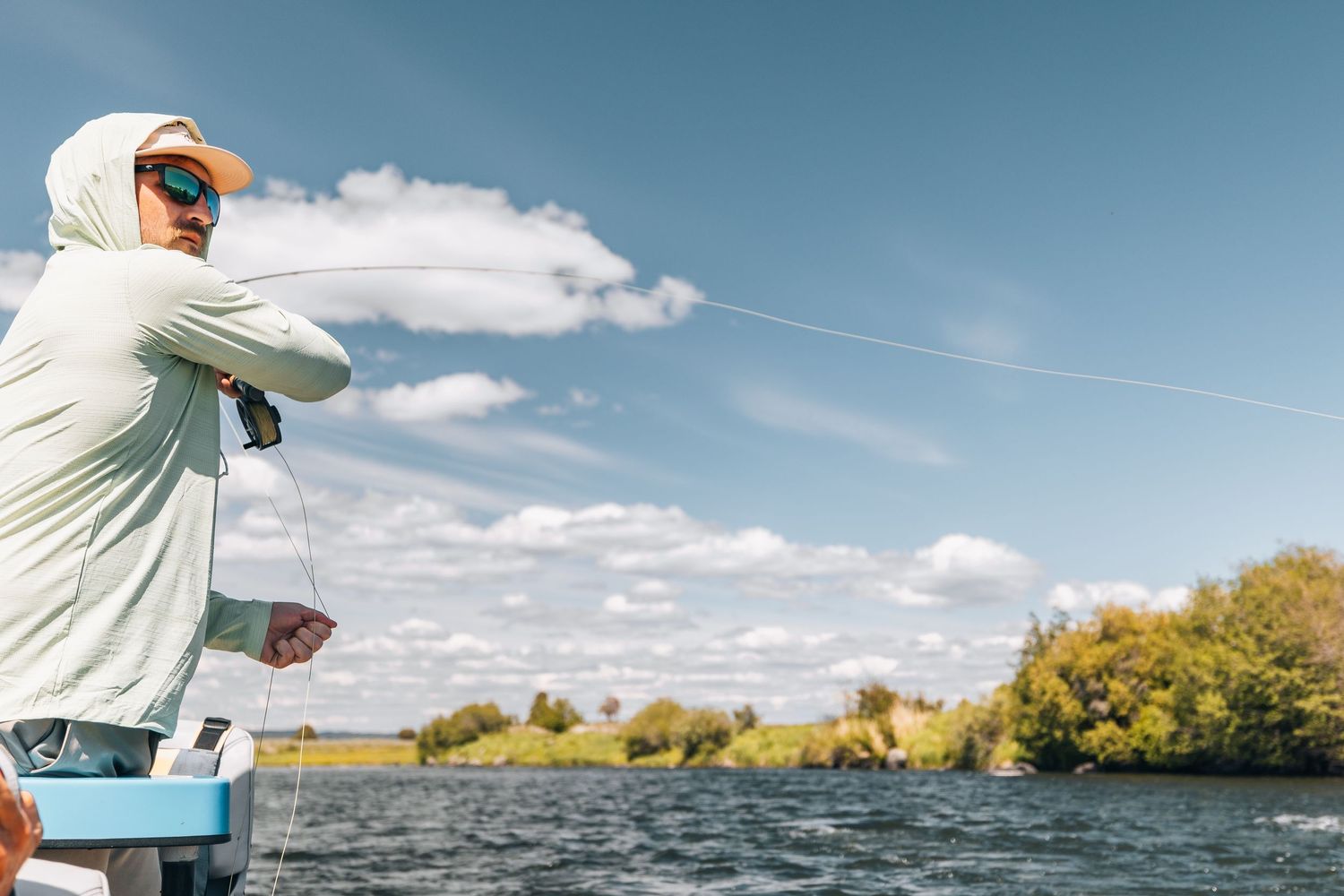 Two people fly fishing on a calm lake surrounded by trees on a sunny autumn day.