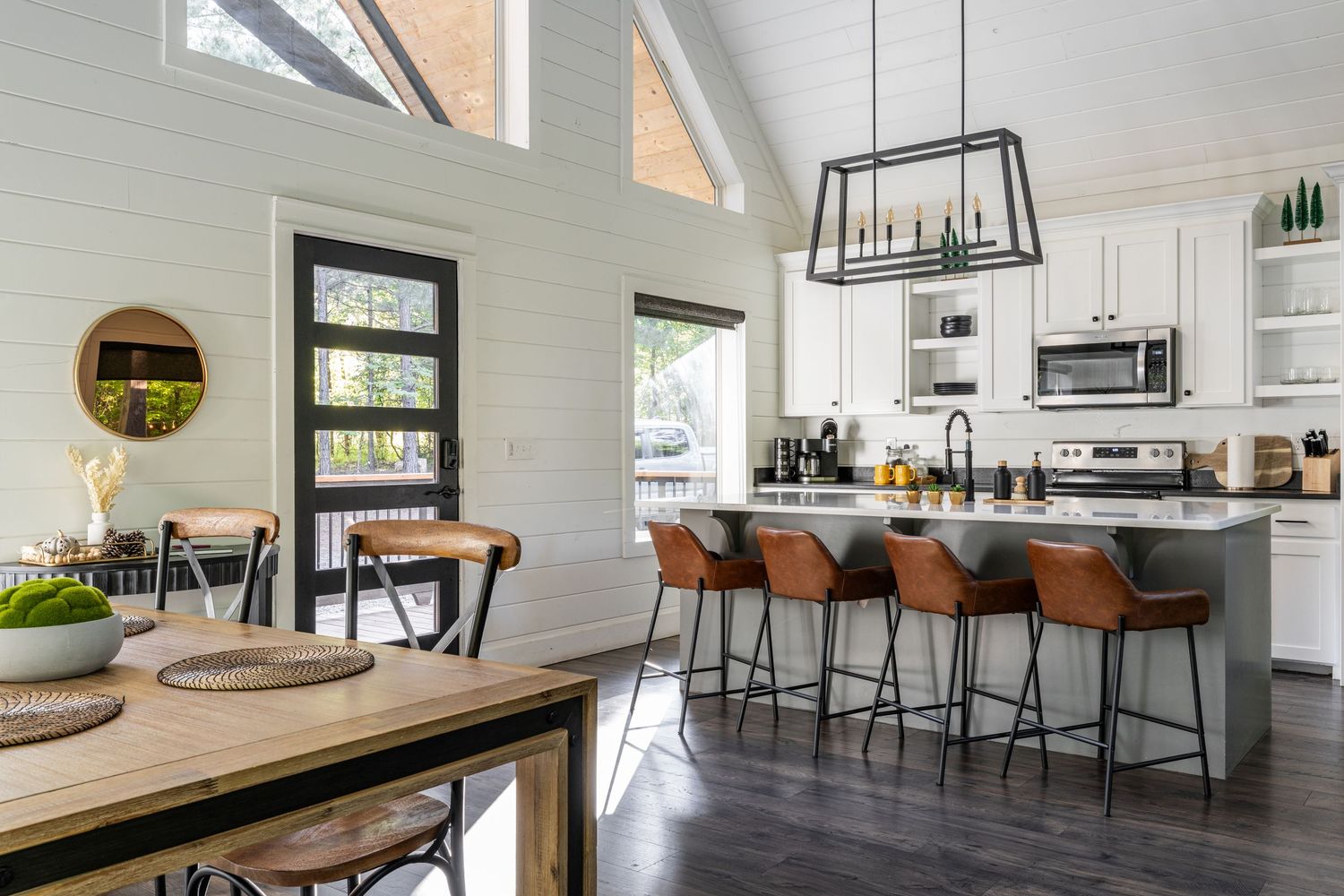 Modern open concept kitchen and dining area with white cabinets, brown leather barstools, and dark hardwood floors.