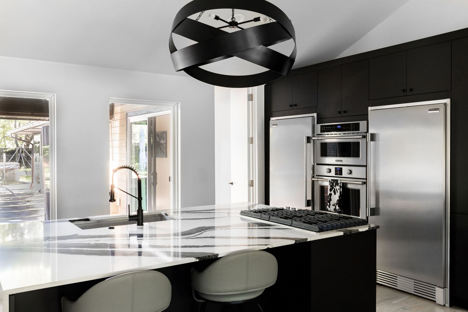 Modern black and white kitchen with sleek island, pendant light, and stainless steel appliances.