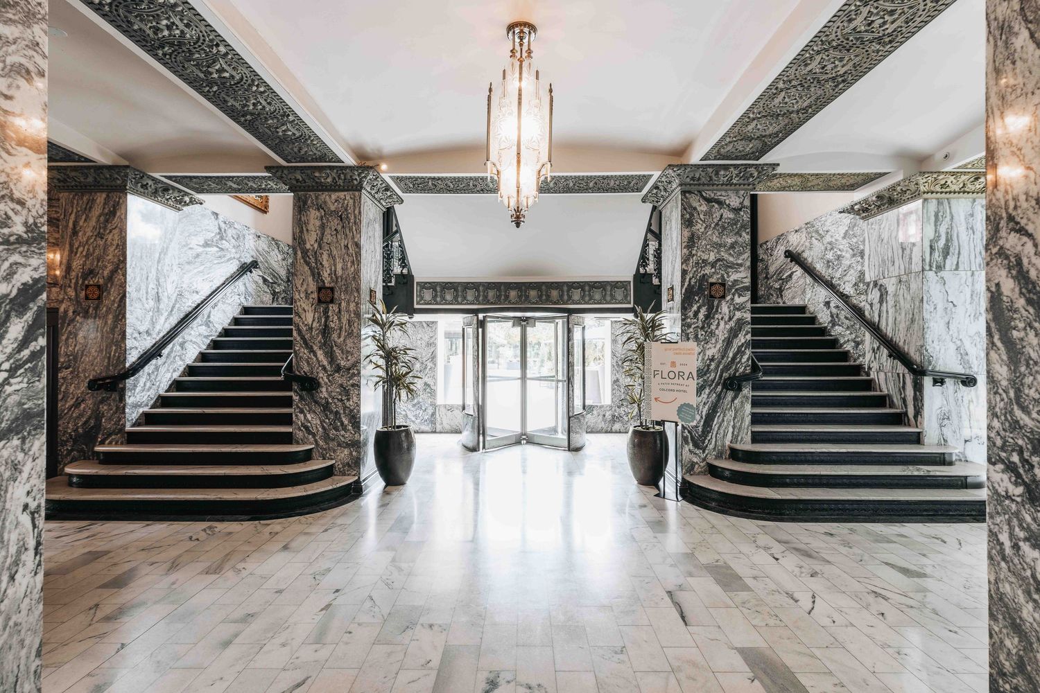 Grand entrance hall with symmetrical marble staircases and art deco lighting fixture.