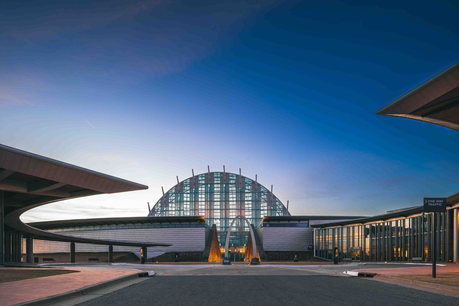 Modern airport terminal building with curved glass dome and geometric architecture under blue sky at dusk.