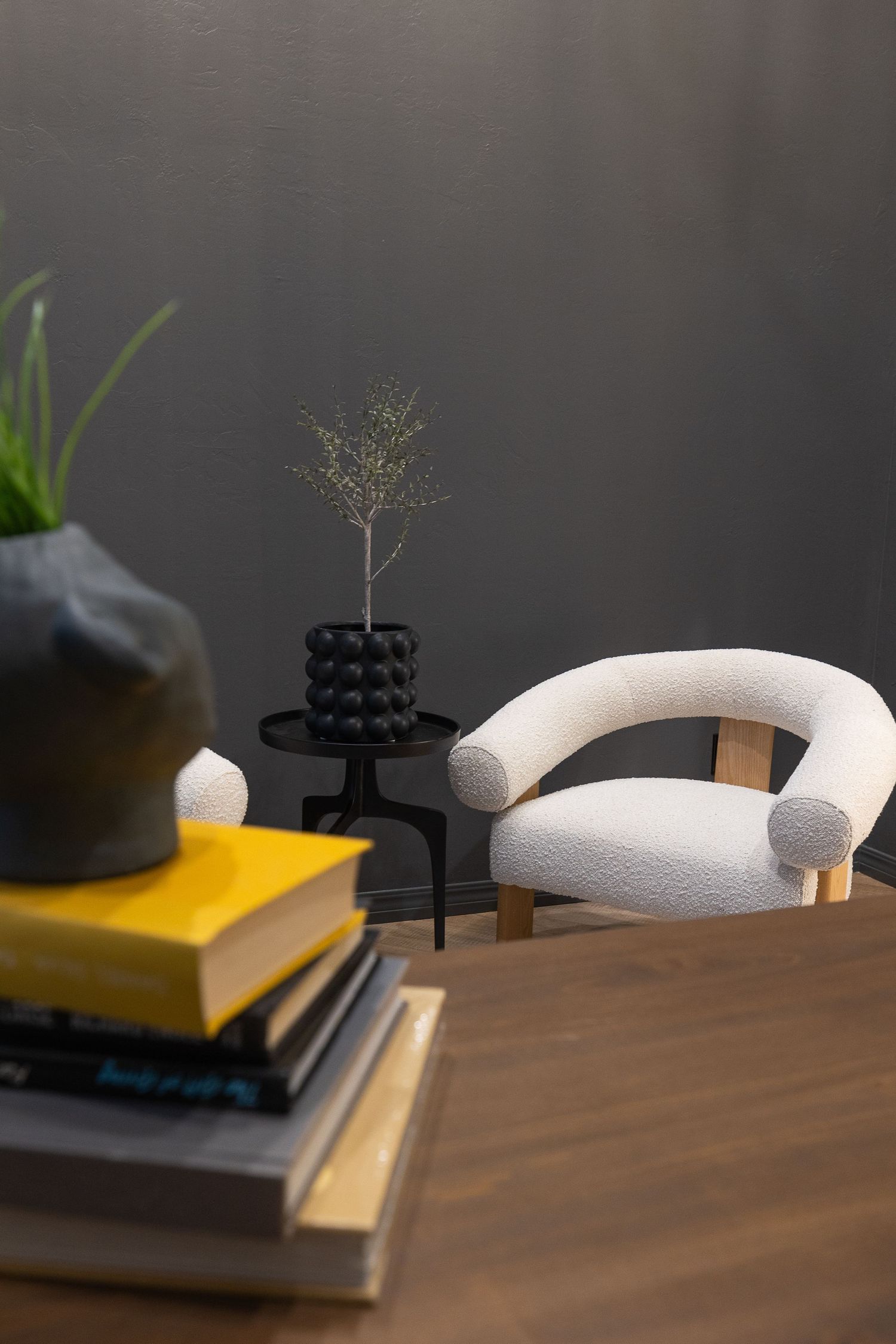 Modern interior decor with a plush cream armchair, stacked books on yellow surface, and minimalist black vase with plant.
