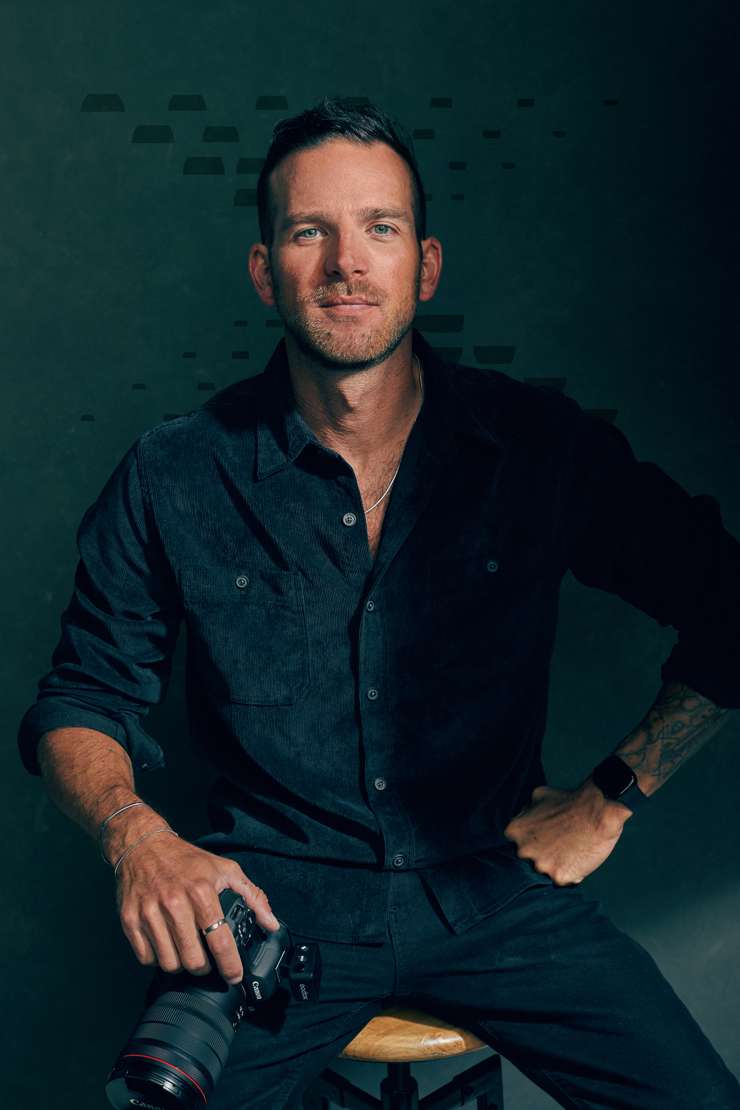 Portrait of photographer with camera against dark green studio backdrop.